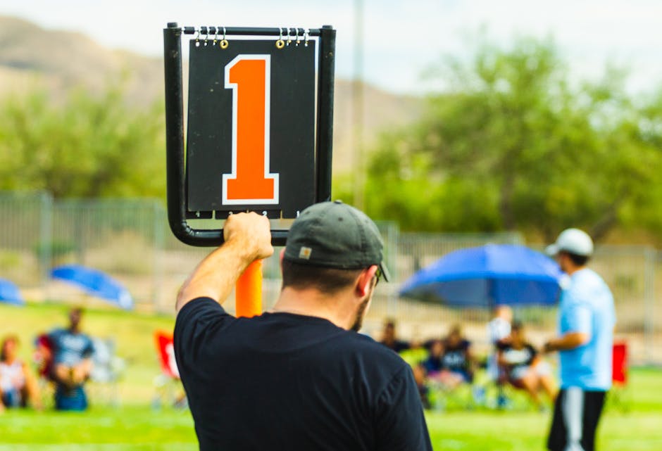 Back view of anonymous male trainer standing near scoreboard on blurred background of field during sports competition